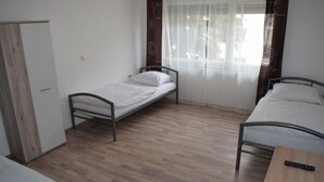 Een kleine, schone kamer met twee eenpersoonsbedden, een houten vloer, een klein tafeltje en een kledingkast.