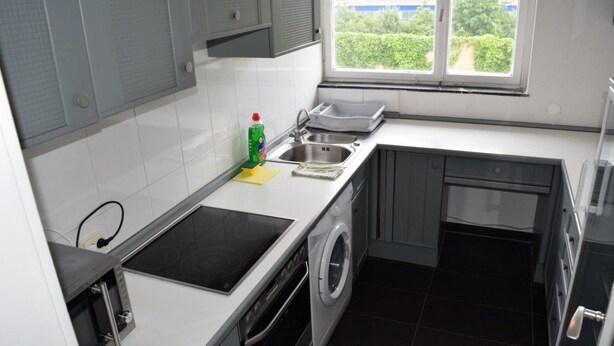 Een kleine keuken met een inbouw wasmachine, een spoelbak en een raam met uitzicht op groen.
