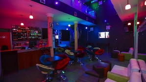 A bar area with a variety of seating options, including bar stools and cushioned chairs, and a visible bar counter stocked with bottles. - Nexus Suites (Lagos)