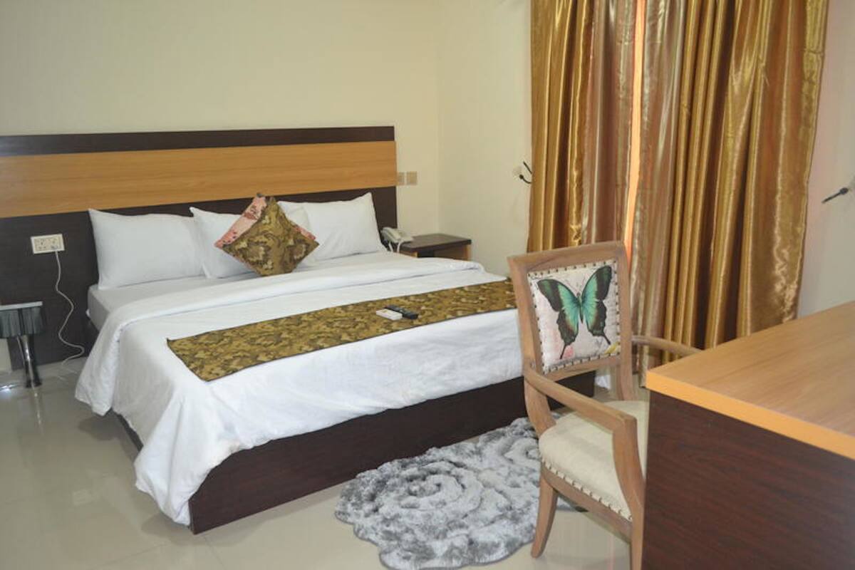 A hotel room with a bed, a wooden nightstand, a chair, and a desk.