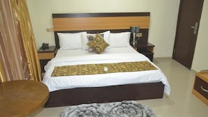 A hotel room with a bed, bedside tables, a round table, and a decorative rug. - Nexus Suites (Lagos)