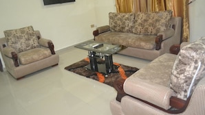 A living room with two armchairs, a sofa, and a glass coffee table. - Nexus Suites (Lagos)