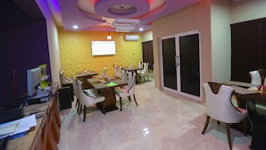 A conference room with a large screen, multiple tables, and chairs. - Nexus Suites (Lagos)