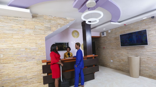 A reception area with a modern design, featuring a stone wall, a reception desk, and a large flat-screen TV mounted on the wall. - Nexus Suites (Lagos)