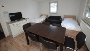 A small, clean room with a wooden table, two beds, a TV, and a window. - AB Apartment 15 (Stuttgart)