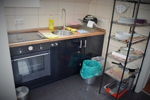 A compact kitchen with a sink, stove, oven, and a metal shelf unit with dishes.