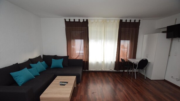 Un salon moderne avec un canapé noir, des coussins turquoise, une table basse en bois et un coin repas comprenant une petite table et des chaises.