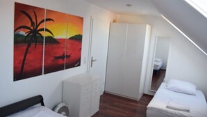 Une chambre à coucher comprenant un lit, une armoire, un petit meuble et un tableau représentant un coucher de soleil sur l’eau.