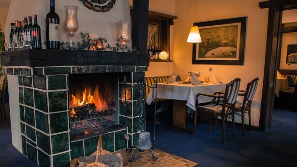A cozy dining area with a fireplace, a table set for two, and a painting on the wall. - Landhotel Laarmann (Lennestadt)
