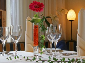 A table set for dining with empty wine glasses, a tall glass with a red flower, and a green plant. - Landhotel Laarmann (Lennestadt)