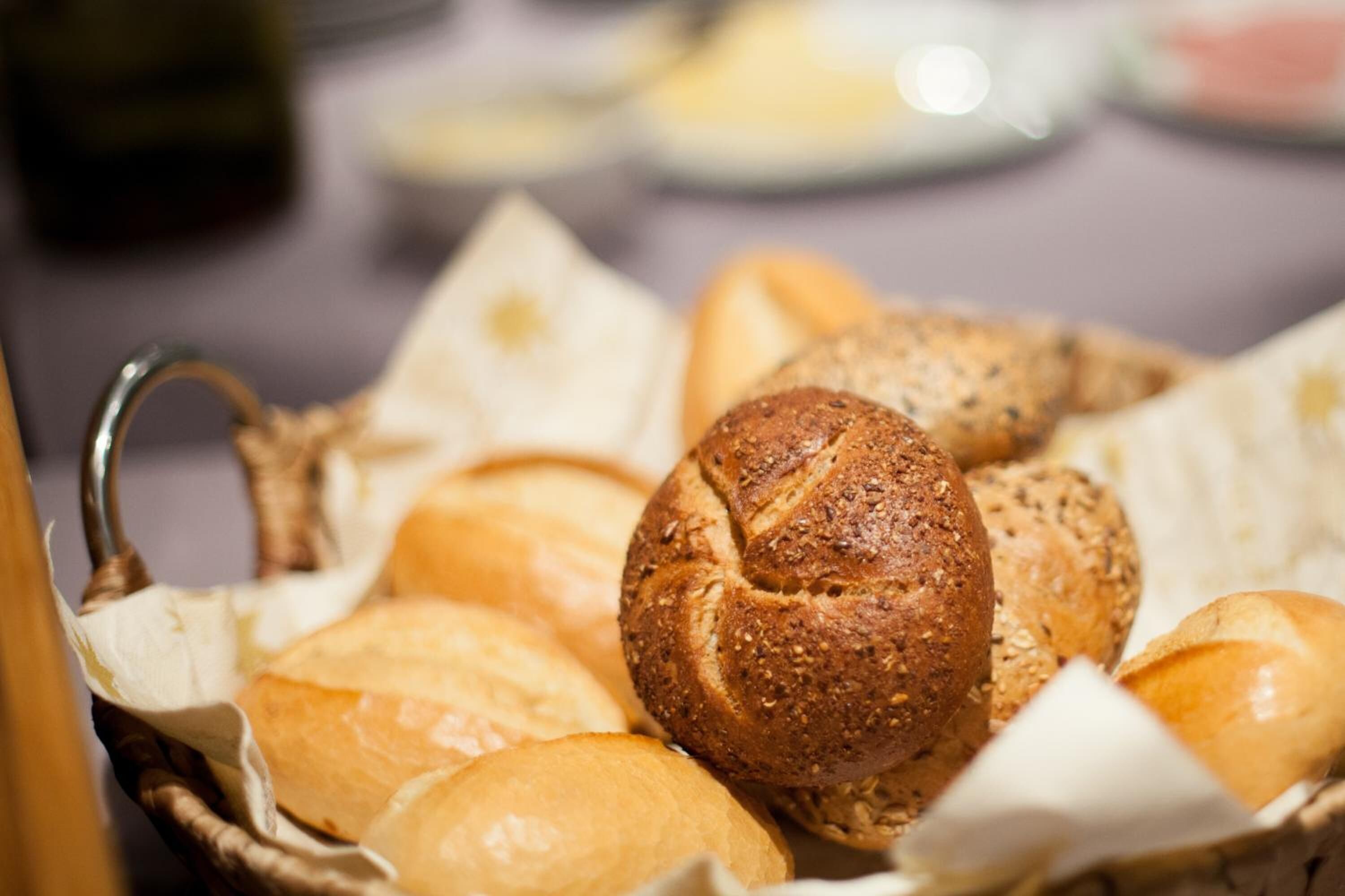 A basket of various breads, including a whole grain loaf and a baguette, on a table.