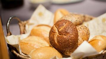 A basket of various breads, including a whole grain loaf and a baguette, on a table.