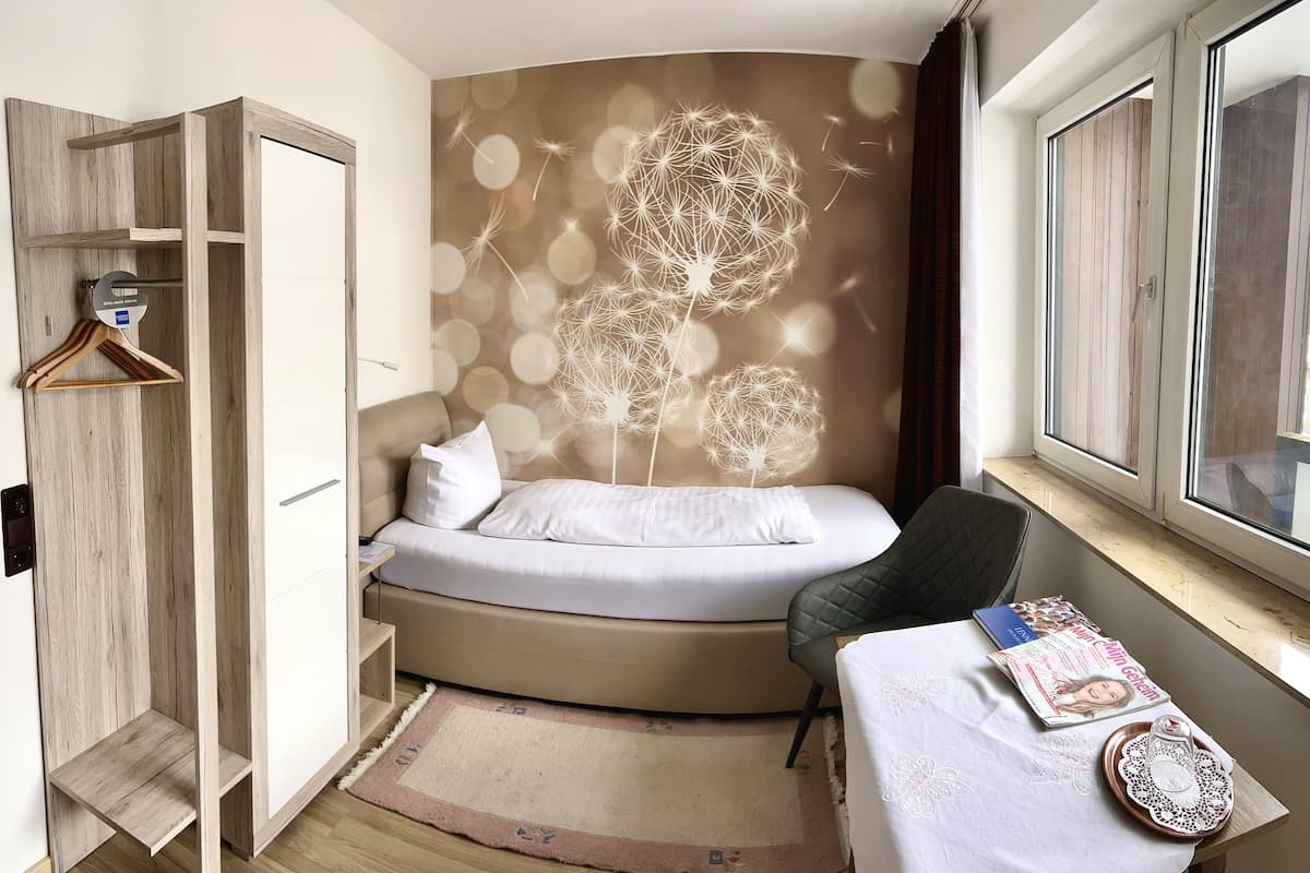 A bedroom with a curved bed, a wooden wardrobe, a desk with a laptop, and a window with a view.