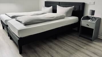 A double bed with a dark headboard and white bedding, a bedside table with a lamp, and a wooden floor.