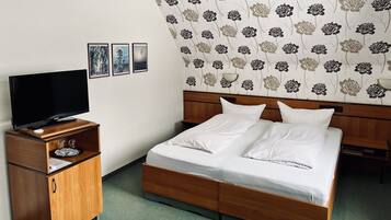 A hotel room with a wooden bed, white bedding, a flat-screen TV on a wooden stand, and a floral wallpaper.