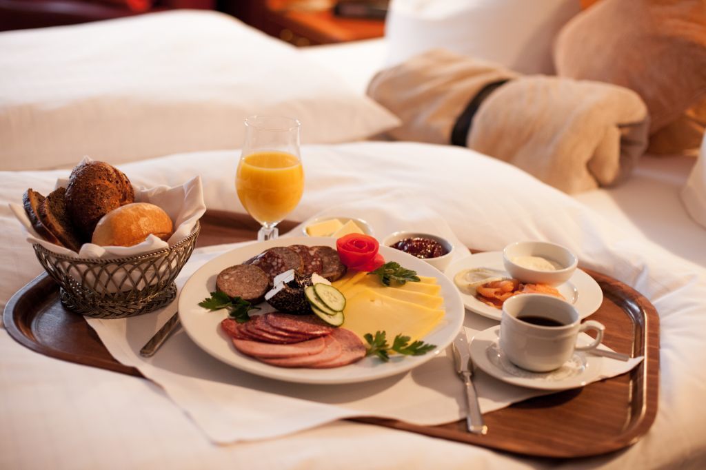 A breakfast tray with eggs, ham, bread, and juice on a bed.