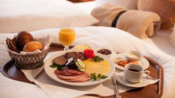 A breakfast tray with eggs, ham, bread, and juice on a bed.