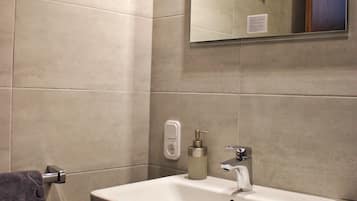 Un baño con lavamanos blanco, un espejo y un perchero para toallas.