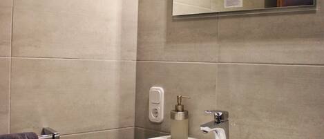 Un baño con lavamanos blanco, un espejo y un perchero para toallas.