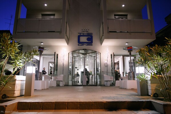 Entrada de hotel con puerta de cristal, un cartel sobre la puerta y algunas personas dentro.