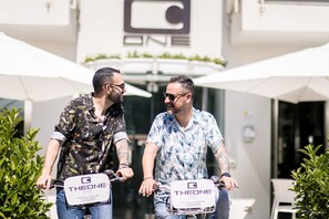 Two men on scooters with 'THEONE' branding, parked in front of a building with a logo above the entrance. - Hotel The One (Riccione)