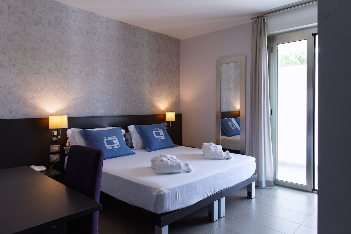 A modern hotel room with a large bed, two bedside lamps, a desk, and a chair.