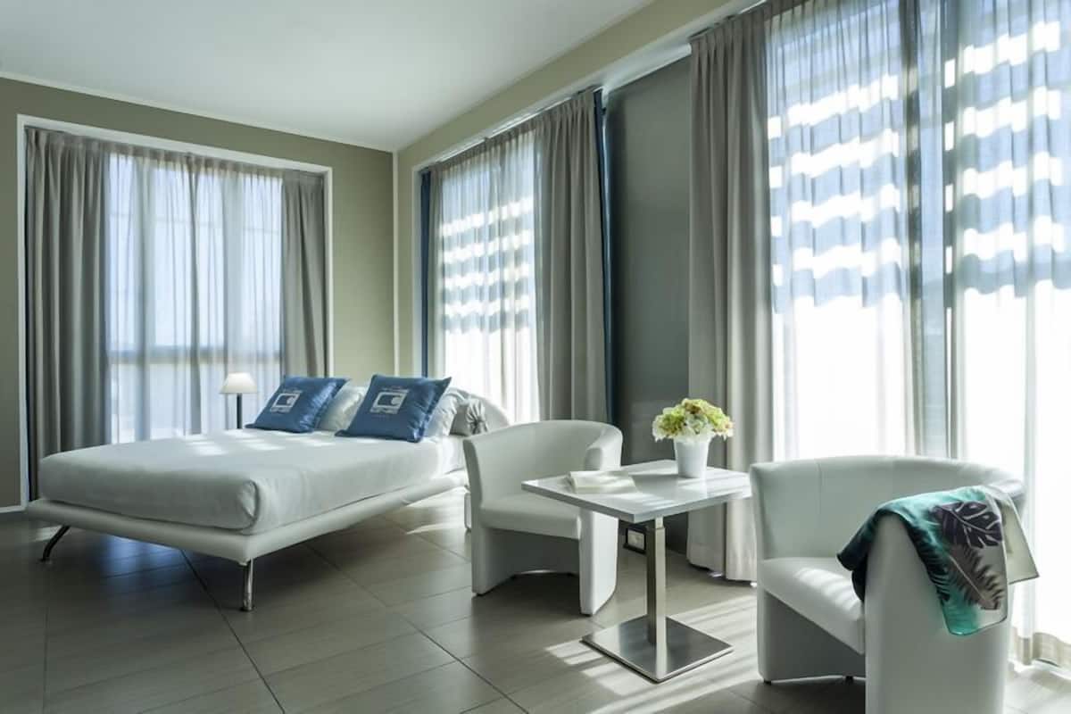 A modern hotel room with a bed, a desk, a chair, and large windows with curtains.