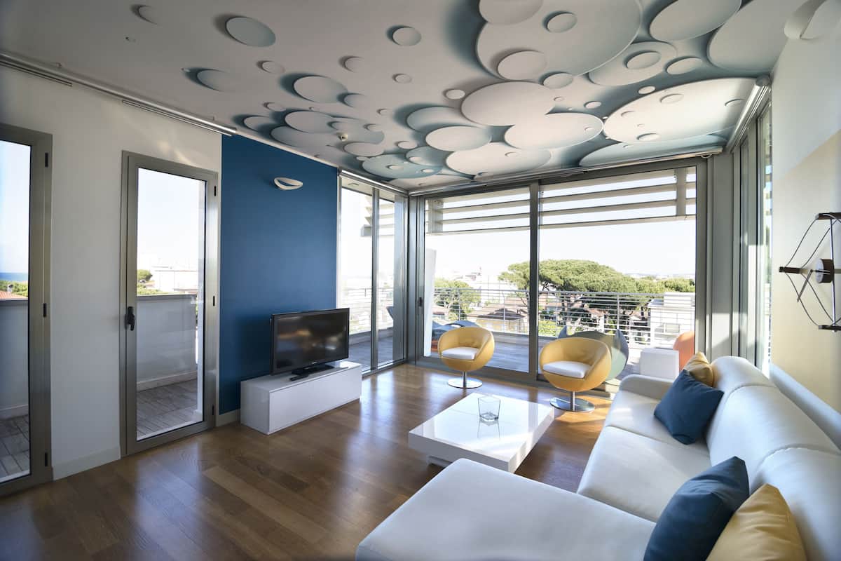 A modern living room with a flat-screen TV, a sofa, two armchairs, and a coffee table.