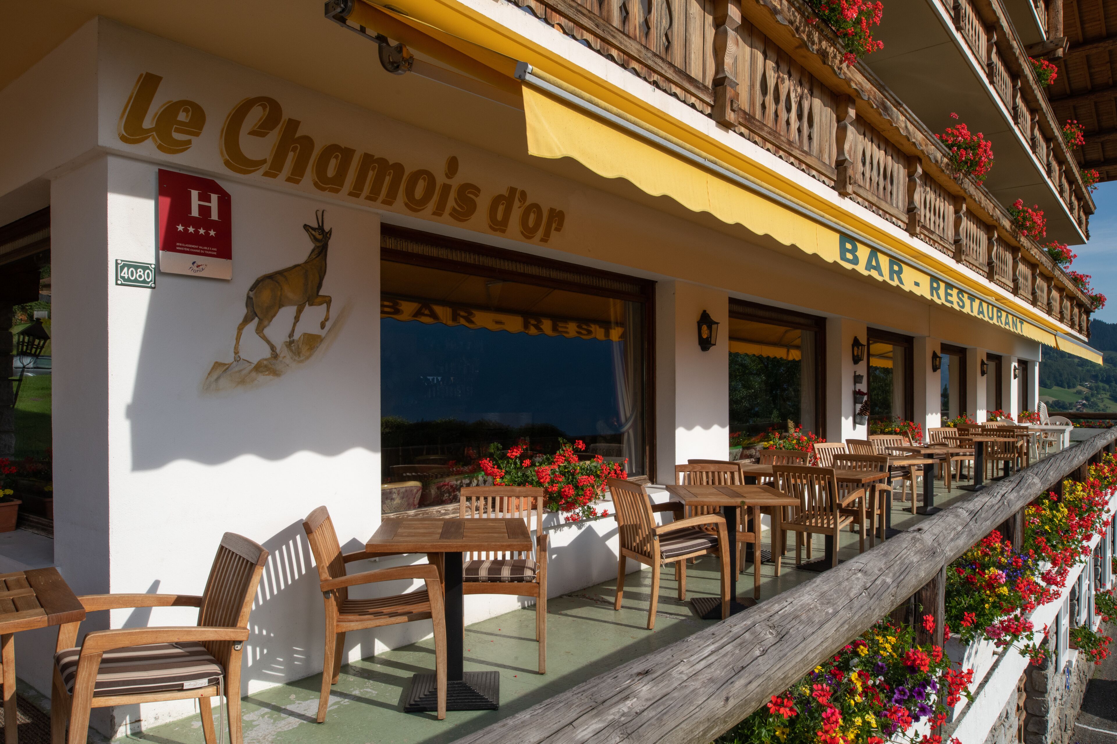 A restaurant with outdoor seating, a sign reading "Le Chamois d'or", and a wooden balcony with flowers.