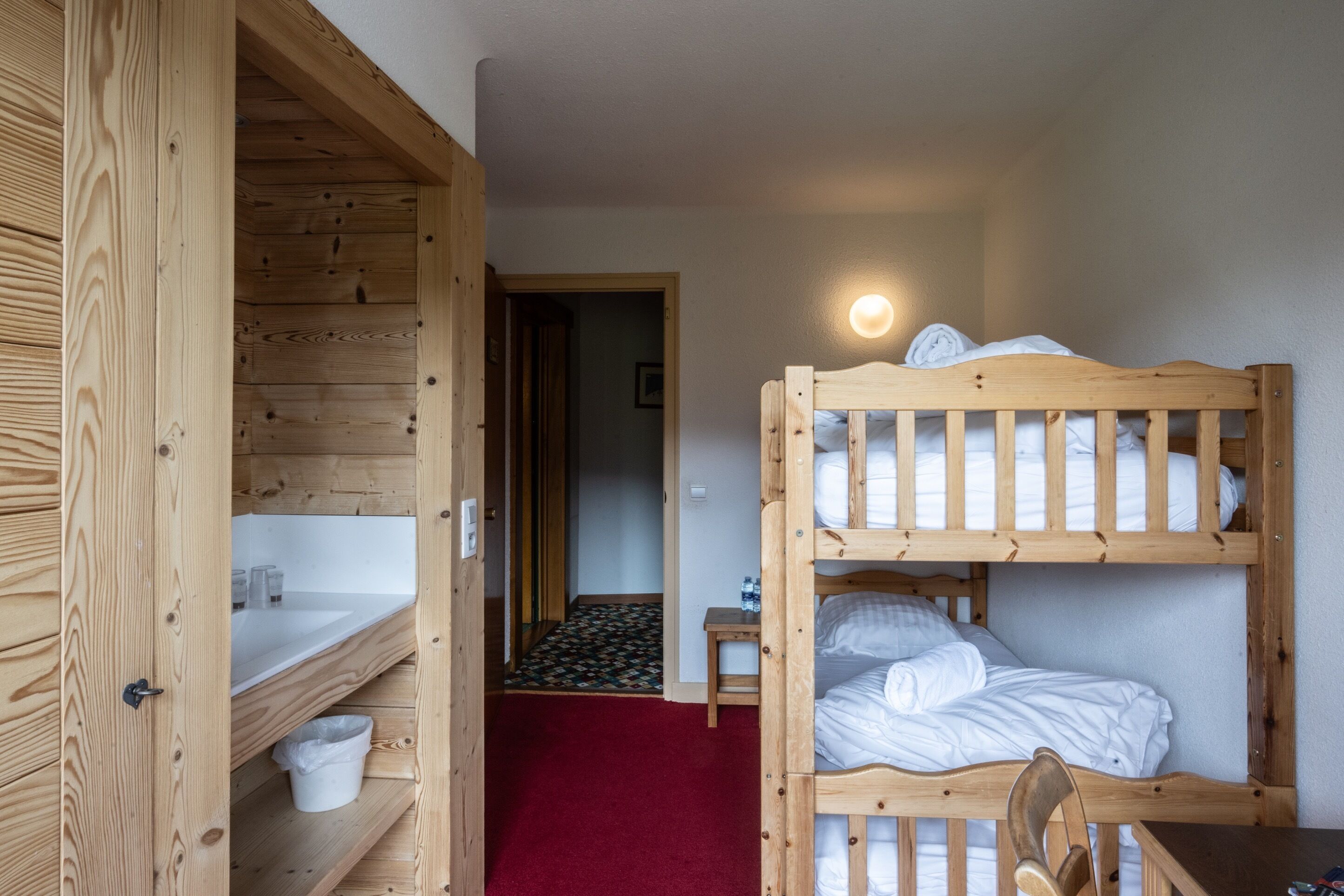 A wooden bunk bed room with a red carpet, a small table, and a sink.