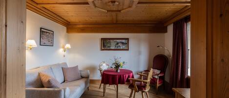 A cozy room with a wooden ceiling, a sofa, a dining table with chairs, and a chair with a red cushion.