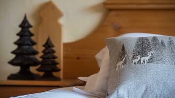 Un lit avec une literie blanche et un oreiller orné d’un motif représentant une scène de forêt.