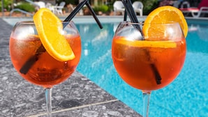 Two glasses of a red beverage with orange slices and straws on a poolside table, with a hotel building in the background. - Le Chamois d'Or (Cordon)