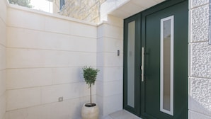 A building exterior with a green door, a potted plant, and a stone wall. - Best Location Rooms (Split)