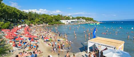 Ein überfüllter Strand mit vielen Sonnenschirmen und Menschen, die das Wasser genießen.