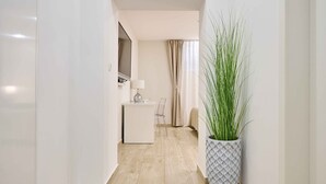 A hallway with a white desk, a chair, a potted plant, and a television mounted on the wall. - Best Location Rooms (Split)