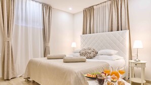 A neatly made bed with a quilted headboard, a bedside table with a lamp, and a tray with breakfast items including croissants, fruit, and orange juice. - Best Location Rooms (Split)