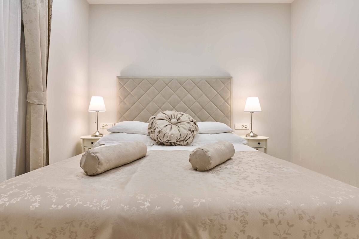 A neatly made bed with a quilted headboard, two bedside lamps, and a decorative pillow.