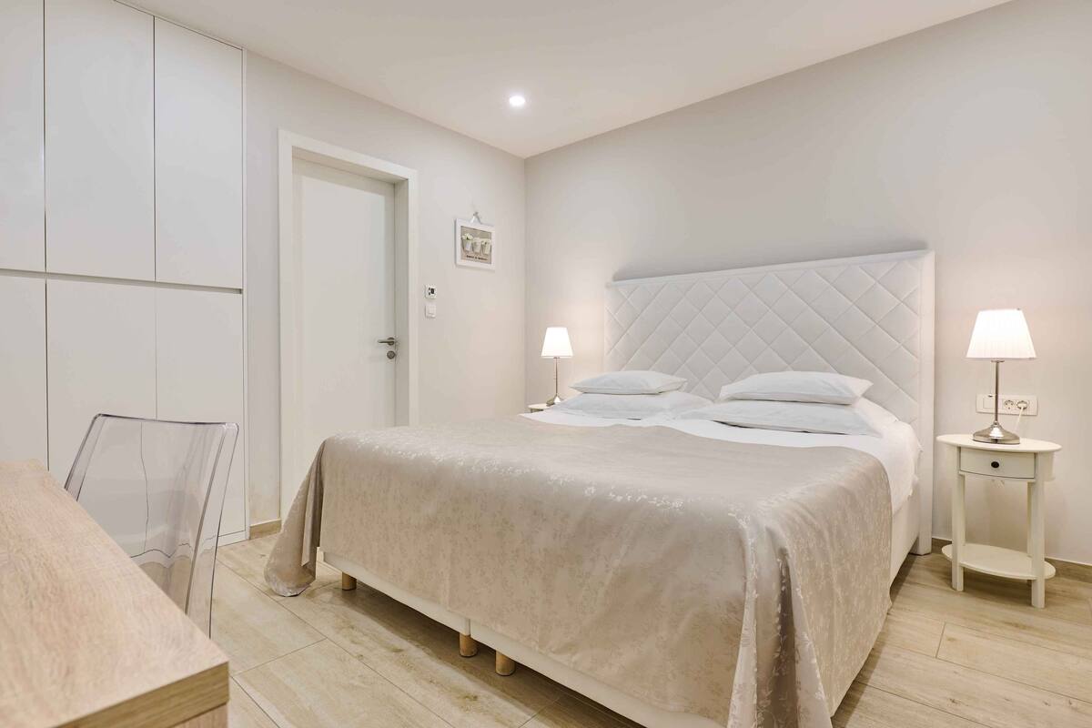 A bedroom with a large bed, two bedside tables with lamps, a door, and a chair.