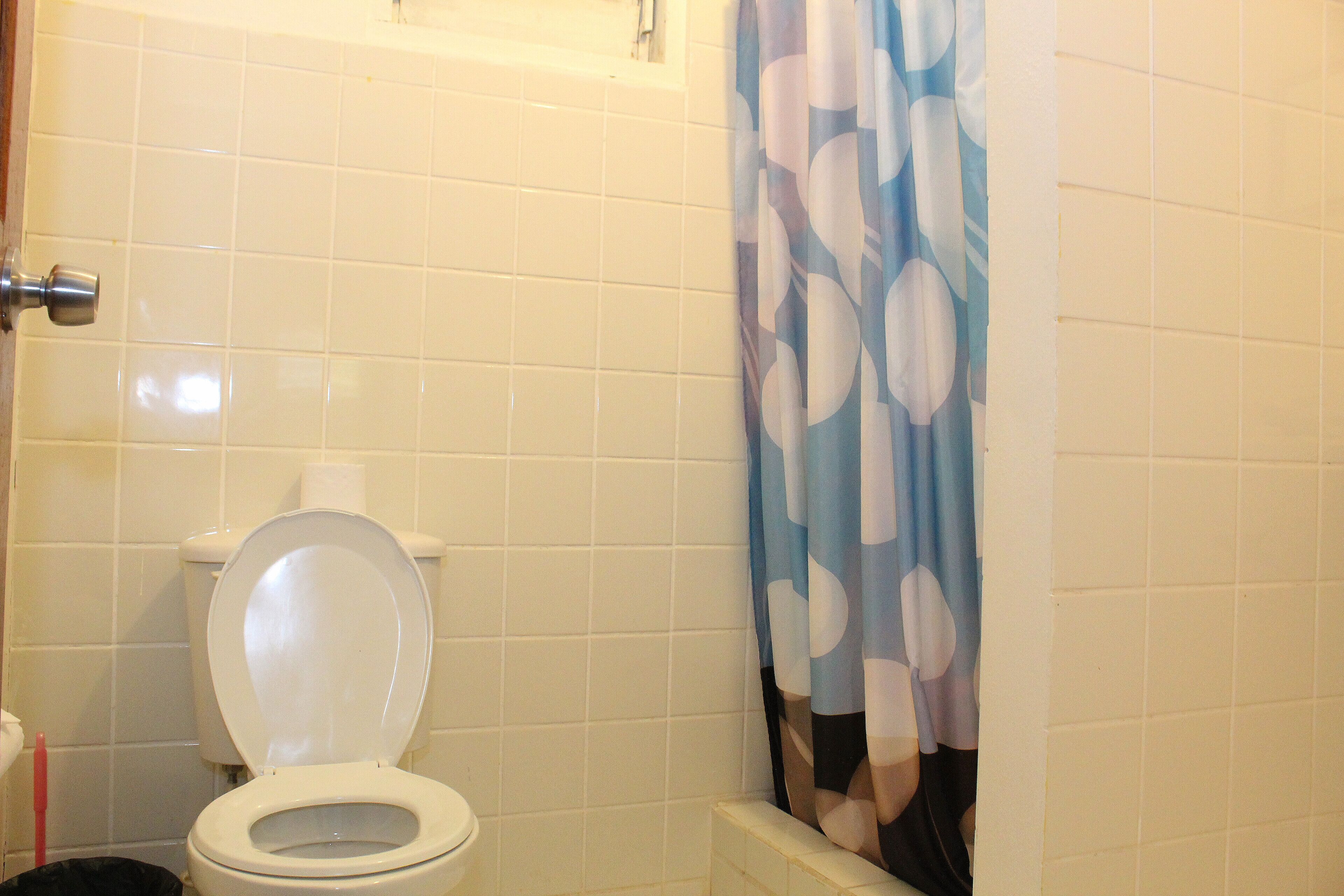 A bathroom with a toilet, a shower curtain, and tiled walls.
