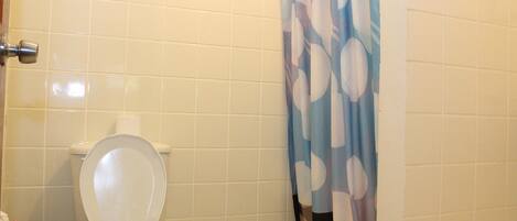 A bathroom with a toilet, a shower curtain, and tiled walls.