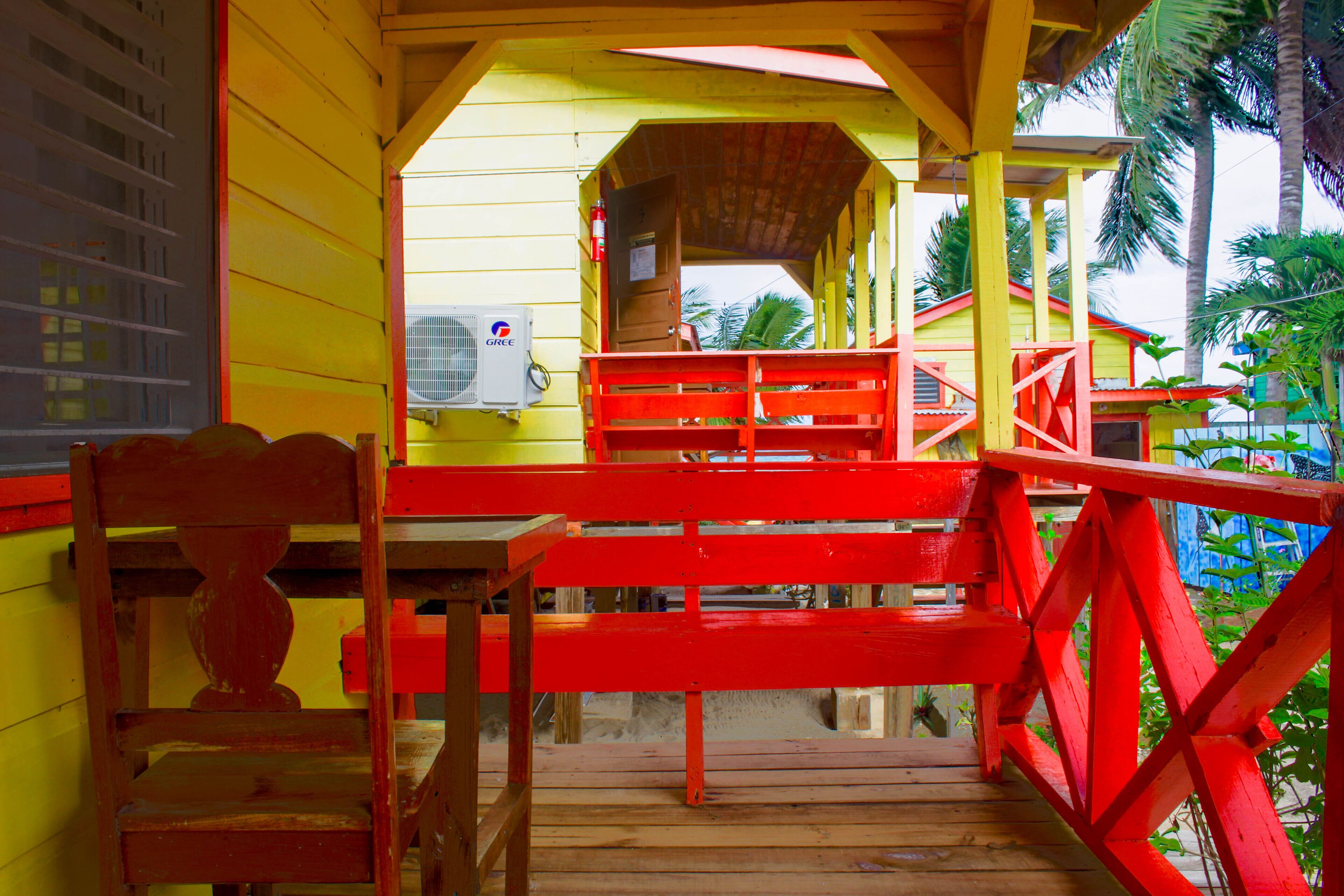 Una escalera de madera con barandas rojas que conduce a un espacio cubierto con vista a palmeras.