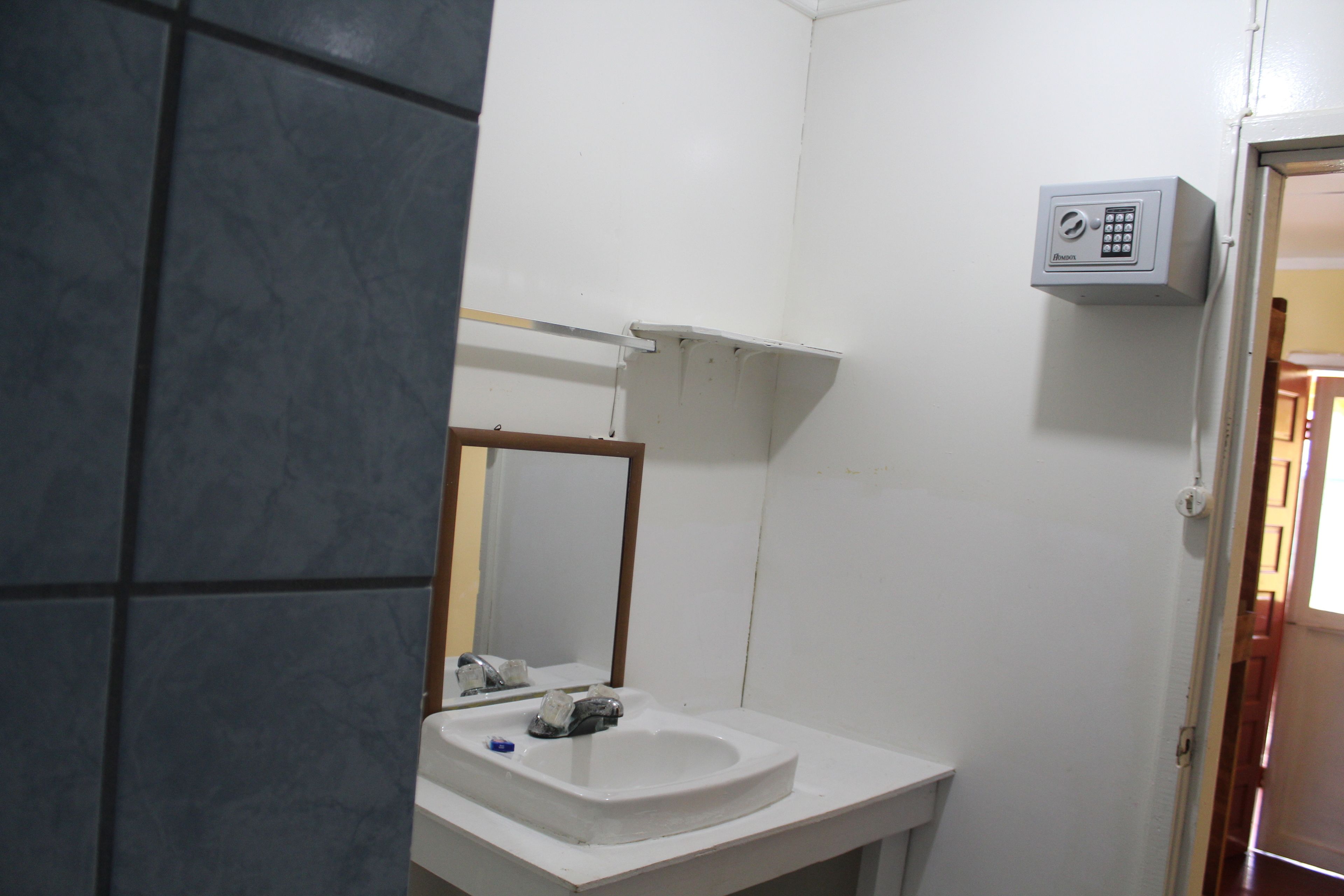 Een badkamer met een witte wastafel, spiegel en een beveiligingsapparaat aan de muur.