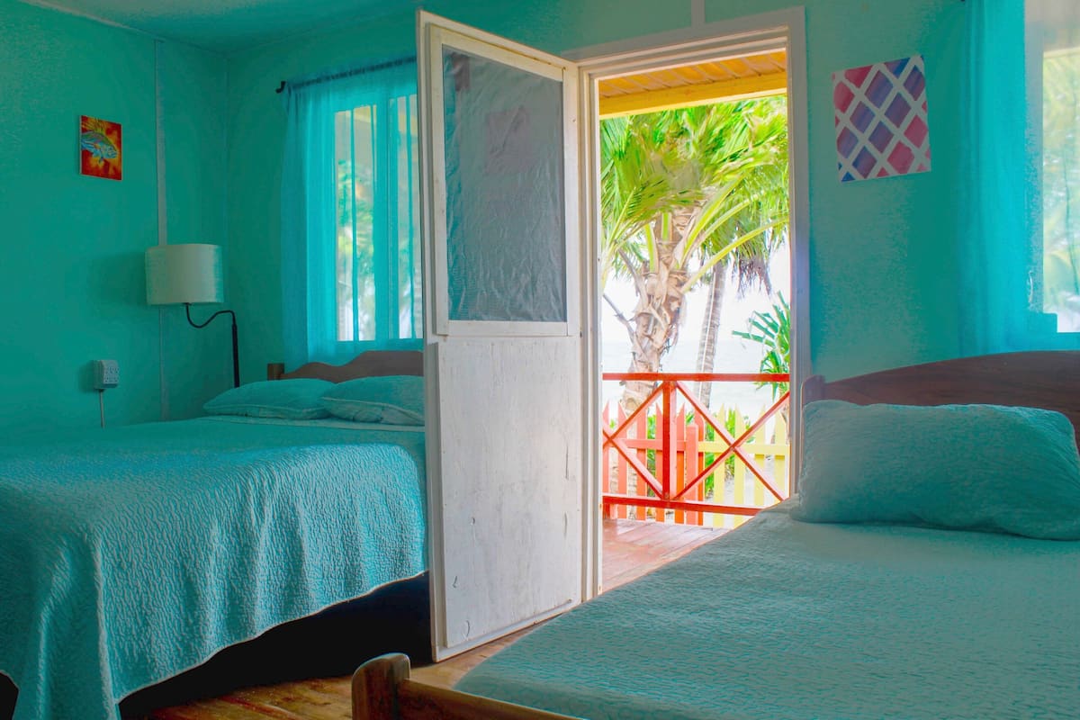 A room with two beds, a window with a view of palm trees, and a door leading to an outdoor balcony.