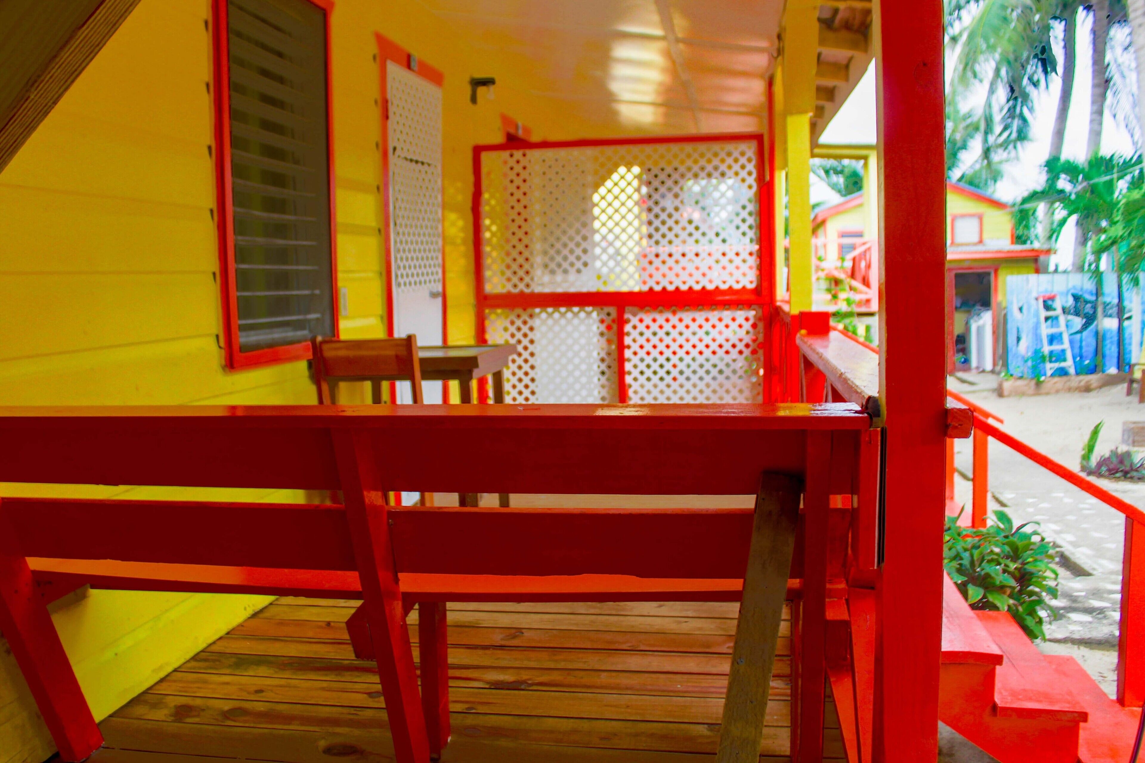 Una terraza de madera con un banco rojo, una puerta blanca y una barandilla roja.