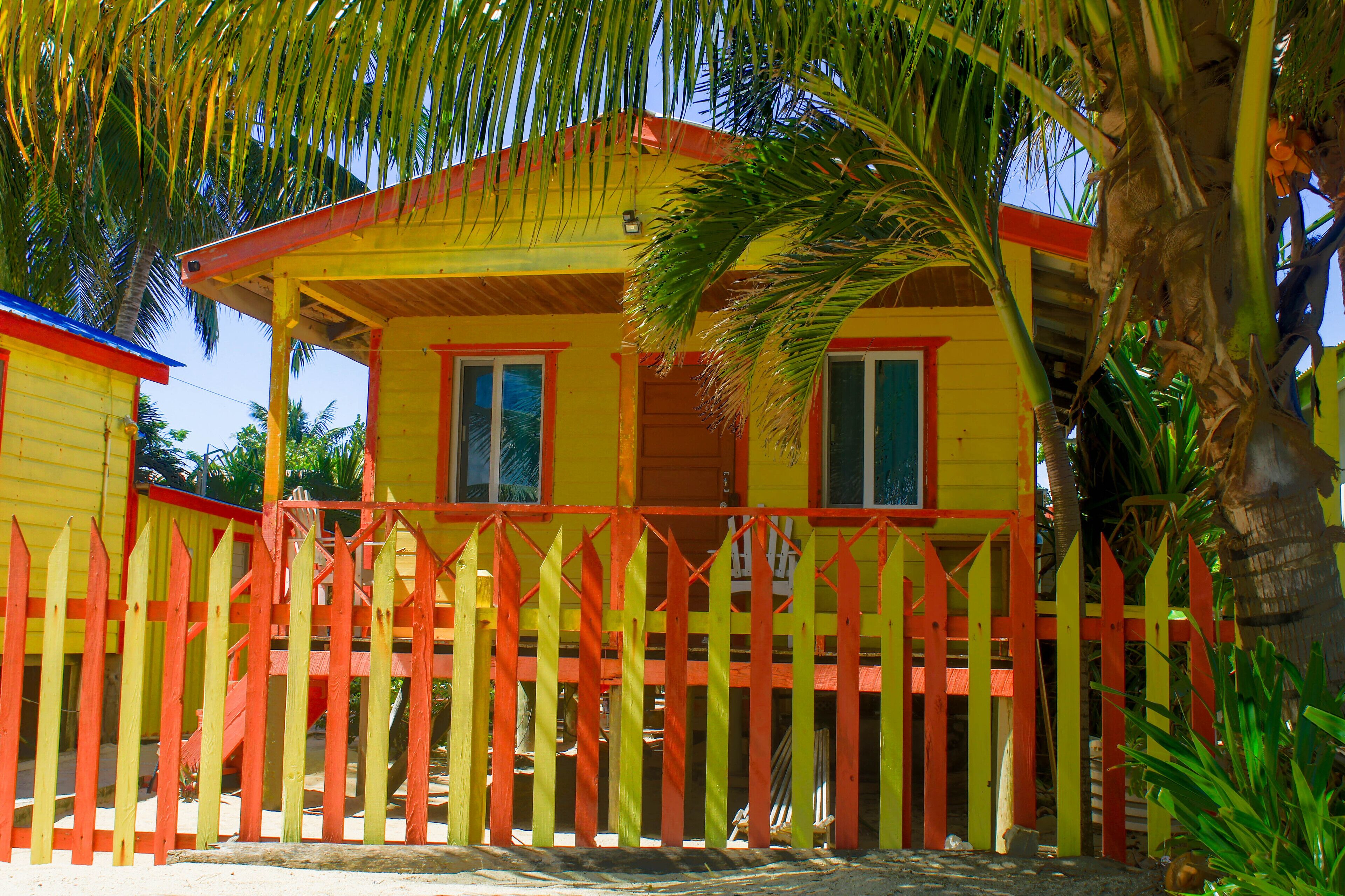 A yellow building with a red and yellow fence, surrounded by palm trees.