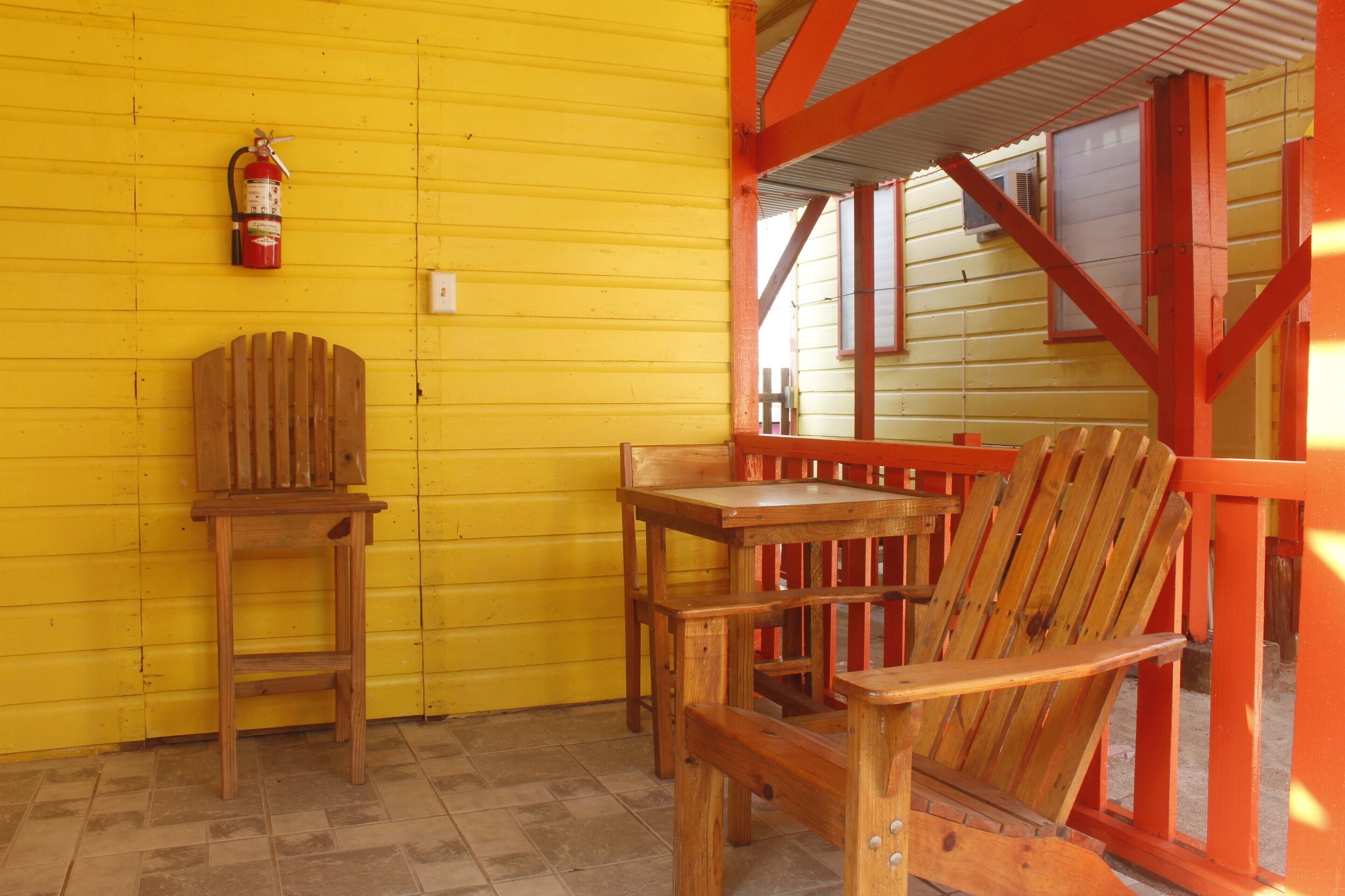 Un ensemble de chaise et de table en bois, placé devant un mur jaune, avec un extincteur fixé sur le mur.
