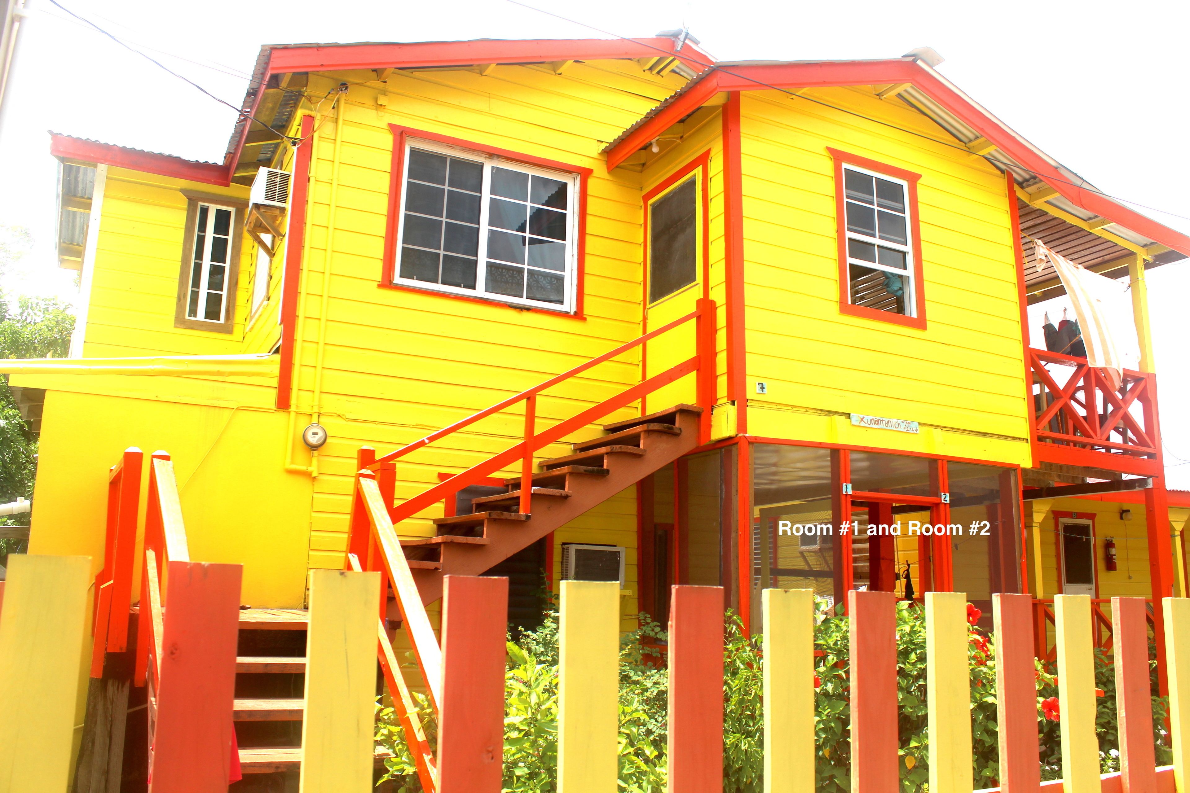 A yellow building with red accents, featuring a staircase and a sign indicating "Room #1 and Room #2".