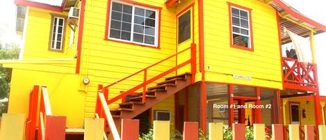 A yellow building with red accents, featuring a staircase and a sign indicating "Room #1 and Room #2".