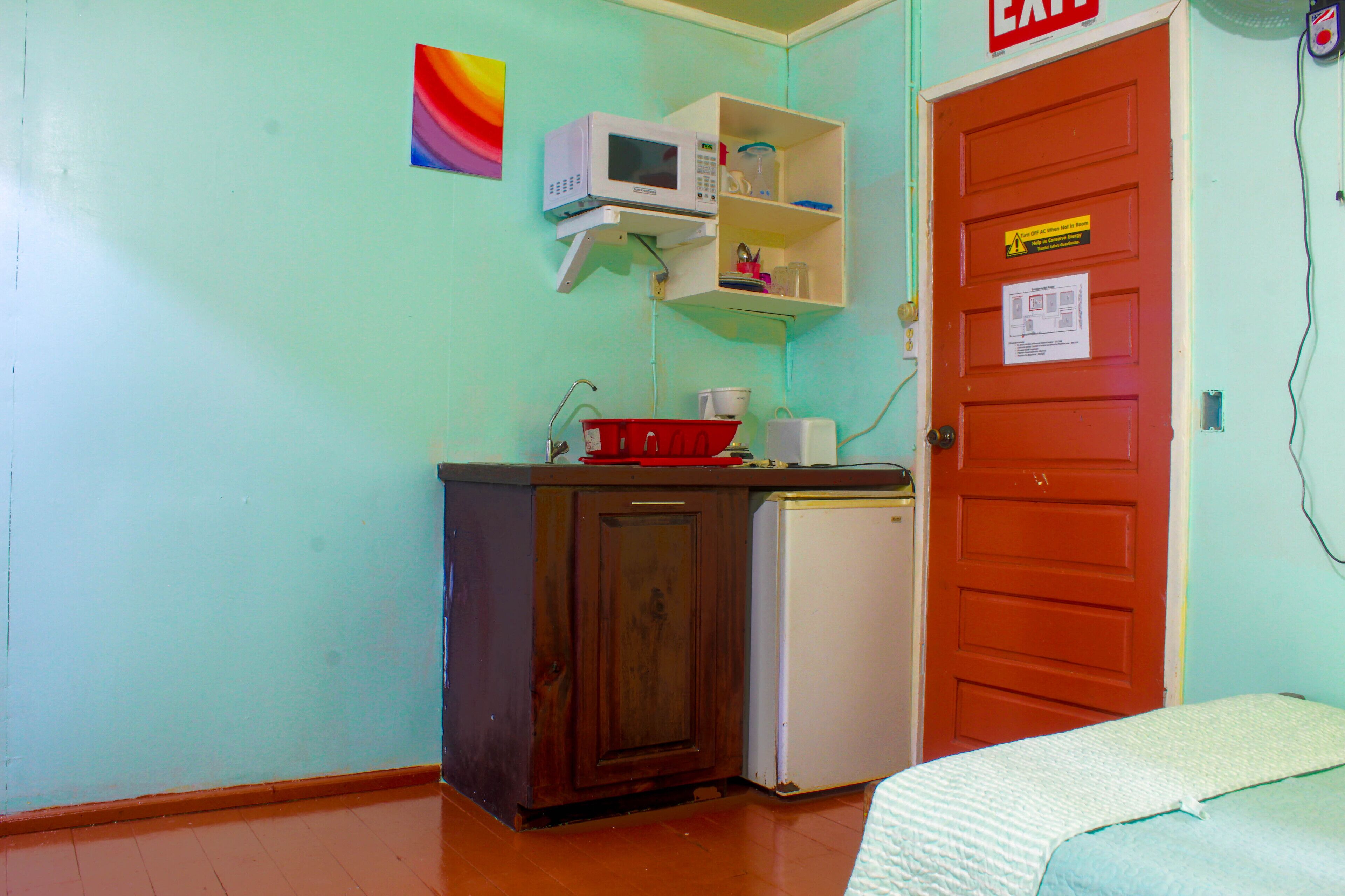 A small kitchenette with a microwave, a refrigerator, and a cabinet. There is a red door with a sign on it.